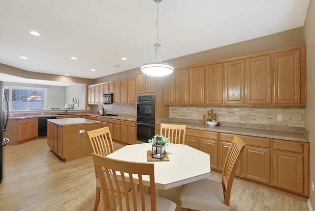 kitchen featuring black appliances, a center island, light hardwood / wood-style floors, decorative light fixtures, and backsplash