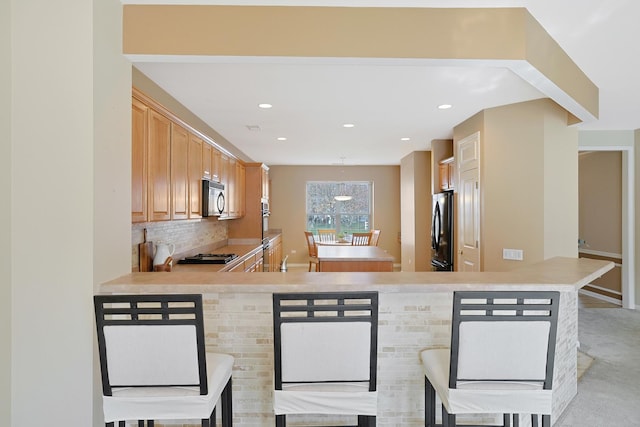 kitchen featuring black appliances, tasteful backsplash, kitchen peninsula, a breakfast bar area, and light brown cabinets