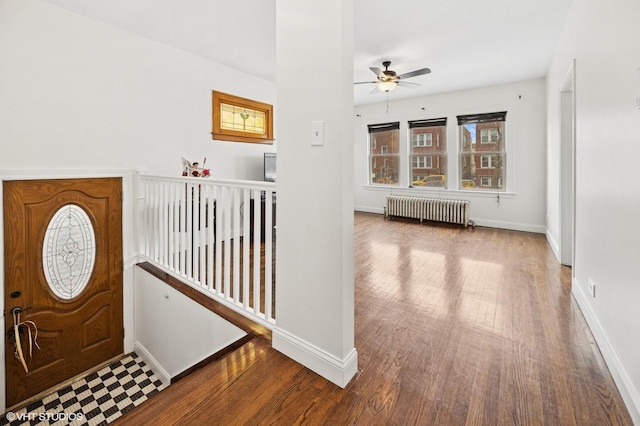 foyer with radiator, ceiling fan, wood-type flooring, and baseboards