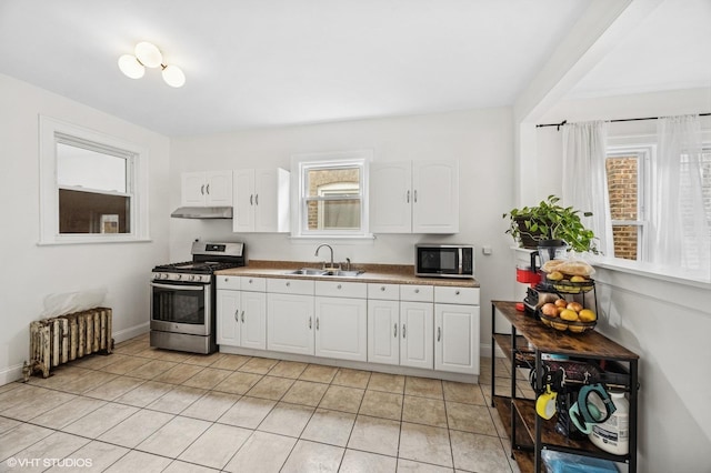 kitchen featuring light tile patterned floors, a sink, white cabinets, appliances with stainless steel finishes, and radiator