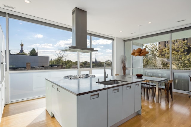 kitchen featuring sink, light hardwood / wood-style flooring, a wall of windows, island exhaust hood, and a center island with sink