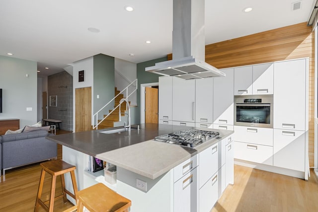 kitchen featuring sink, island range hood, appliances with stainless steel finishes, a kitchen island with sink, and white cabinets