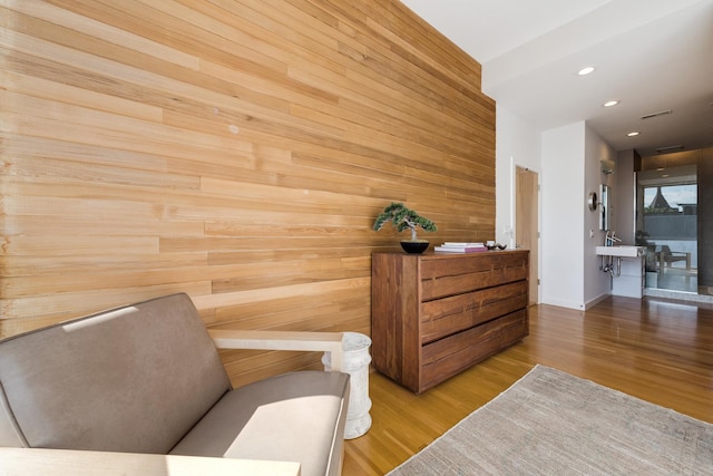 sitting room with hardwood / wood-style floors and wooden walls