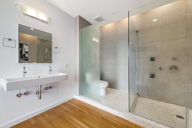 bathroom with hardwood / wood-style floors, a shower with door, sink, and toilet