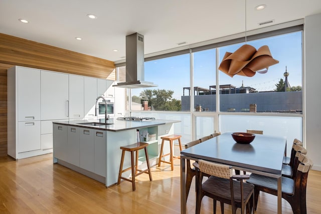 kitchen with a kitchen island with sink, island range hood, expansive windows, and white cabinets