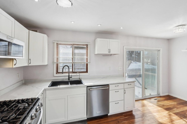 kitchen featuring sink, stainless steel appliances, wood-type flooring, light stone countertops, and white cabinets