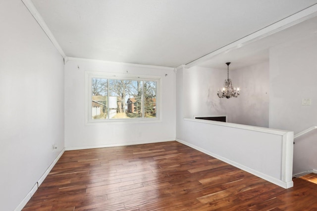 unfurnished room featuring a notable chandelier, dark wood-type flooring, and ornamental molding