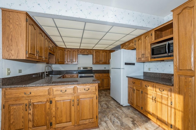 kitchen featuring appliances with stainless steel finishes, a drop ceiling, sink, dark stone countertops, and kitchen peninsula