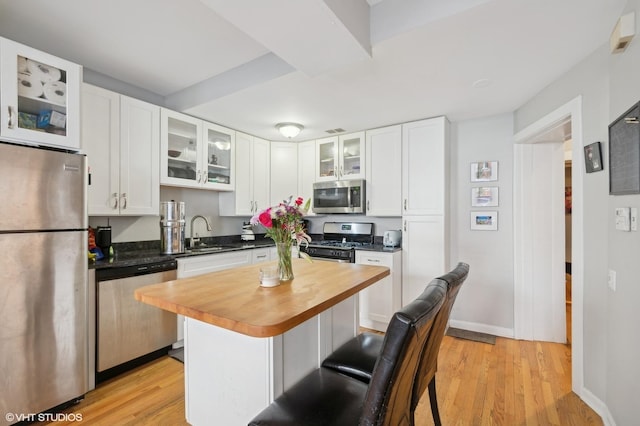 kitchen with a kitchen island, appliances with stainless steel finishes, white cabinetry, sink, and butcher block counters