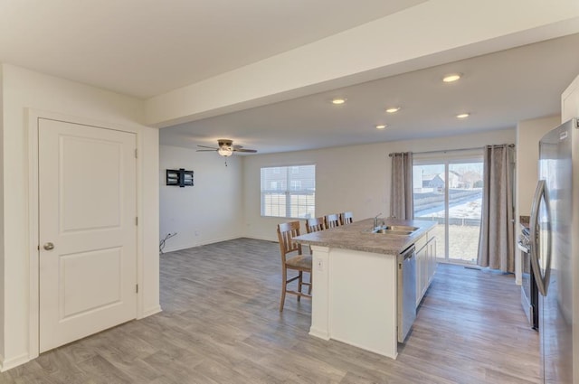 kitchen featuring a kitchen bar, appliances with stainless steel finishes, white cabinetry, a kitchen island with sink, and plenty of natural light