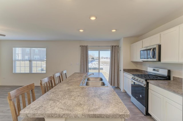 kitchen with light hardwood / wood-style floors, appliances with stainless steel finishes, sink, white cabinets, and a center island with sink