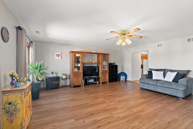 living room featuring light hardwood / wood-style flooring, ceiling fan, and a wood stove