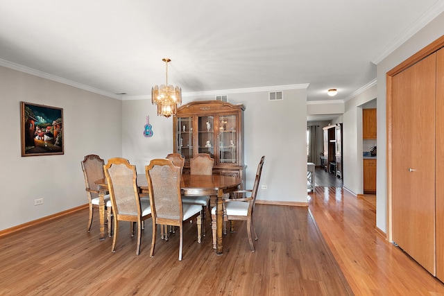 dining area featuring crown molding, light hardwood / wood-style flooring, and a notable chandelier