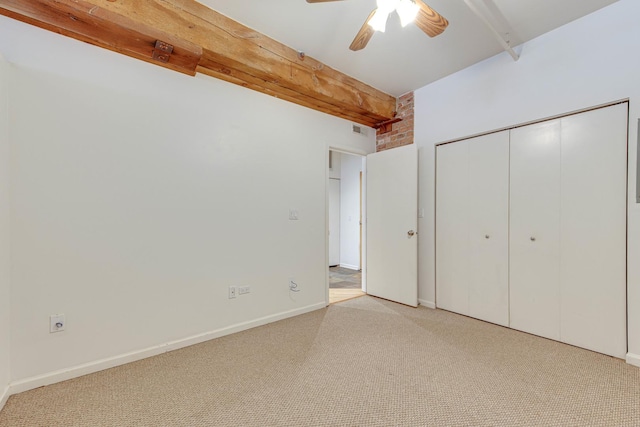 unfurnished bedroom featuring brick wall, a closet, light colored carpet, beam ceiling, and ceiling fan