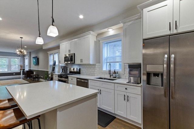 kitchen featuring pendant lighting, white cabinets, stainless steel appliances, sink, and backsplash