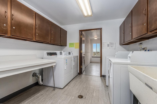 clothes washing area featuring cabinets, sink, washing machine and dryer, and light wood-type flooring