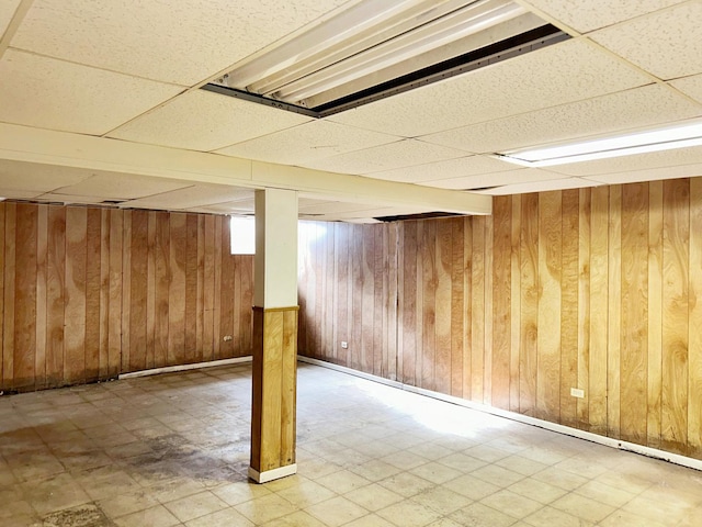 basement featuring wood walls and a drop ceiling