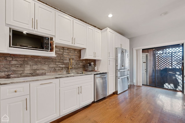 kitchen with light stone countertops, white cabinetry, sink, light wood-type flooring, and stainless steel appliances