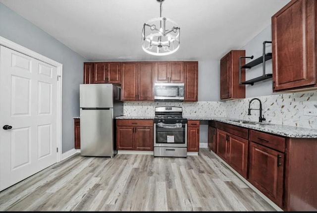 kitchen with appliances with stainless steel finishes, pendant lighting, sink, light stone counters, and light hardwood / wood-style floors