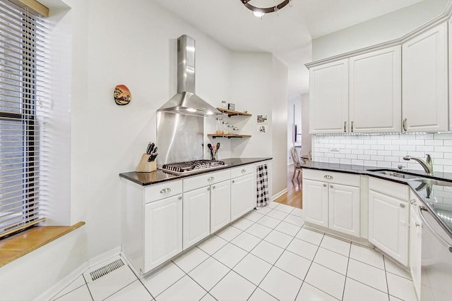 kitchen featuring stainless steel gas stovetop, sink, dishwashing machine, white cabinets, and wall chimney range hood