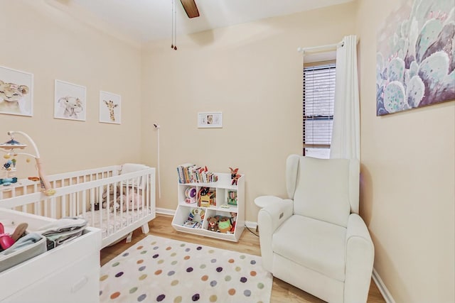 bedroom with ceiling fan, a nursery area, and hardwood / wood-style floors