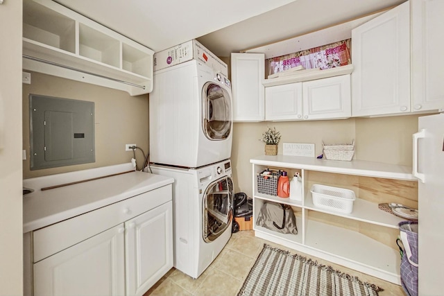 laundry area with electric panel, light tile patterned floors, cabinets, and stacked washer and dryer