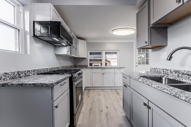 kitchen with light hardwood / wood-style floors, sink, white cabinets, light stone counters, and stainless steel range with gas cooktop