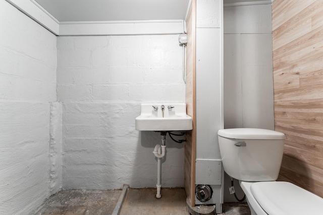 bathroom featuring concrete floors, sink, toilet, and wooden walls