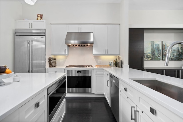 kitchen with built in appliances, sink, white cabinetry, and dark hardwood / wood-style floors