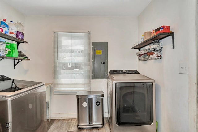 clothes washing area with electric panel, washing machine and dryer, and light wood-type flooring