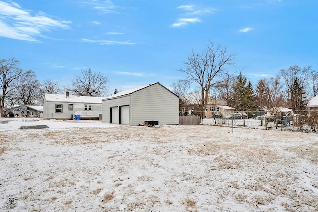 snow covered rear of property with a garage and an outbuilding