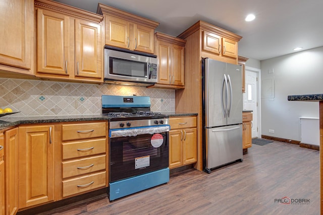 kitchen featuring appliances with stainless steel finishes, dark hardwood / wood-style floors, tasteful backsplash, and dark stone countertops