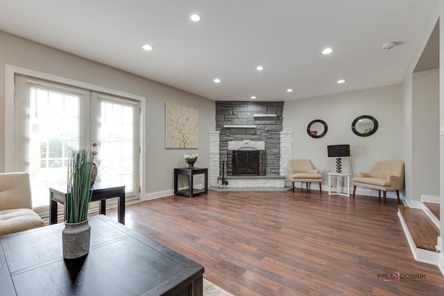 living room with a stone fireplace and dark wood-type flooring