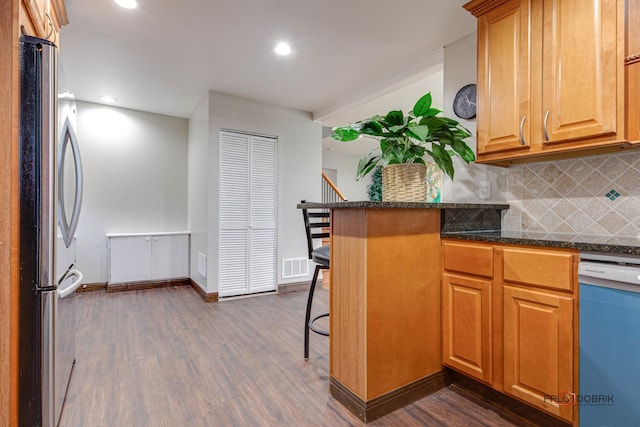 kitchen featuring a kitchen bar, tasteful backsplash, dishwasher, dark wood-type flooring, and stainless steel fridge