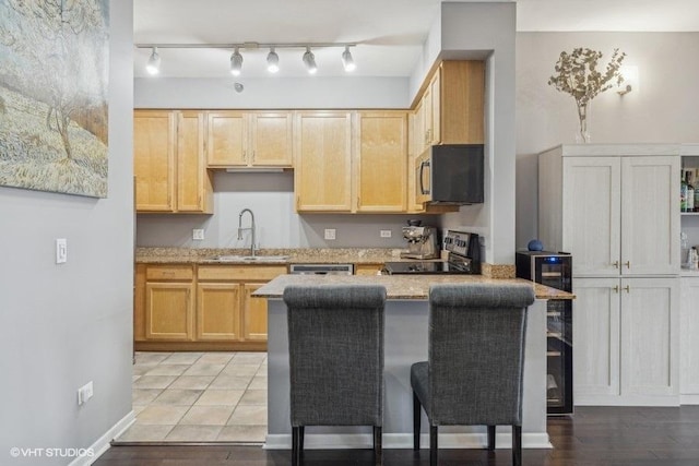 kitchen with light brown cabinets, sink, light stone countertops, a breakfast bar area, and stainless steel appliances