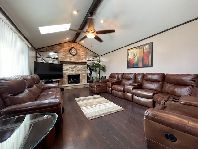 living room featuring a brick fireplace, dark wood-type flooring, vaulted ceiling with skylight, and ceiling fan