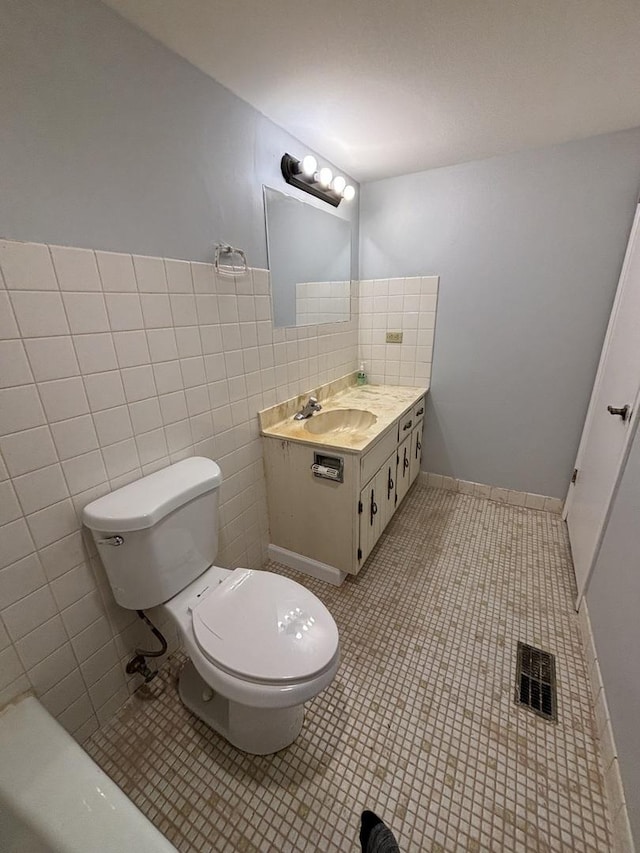 bathroom with toilet, tile patterned flooring, vanity, and tile walls