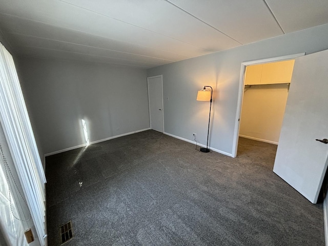 unfurnished bedroom featuring a spacious closet, a closet, and dark colored carpet