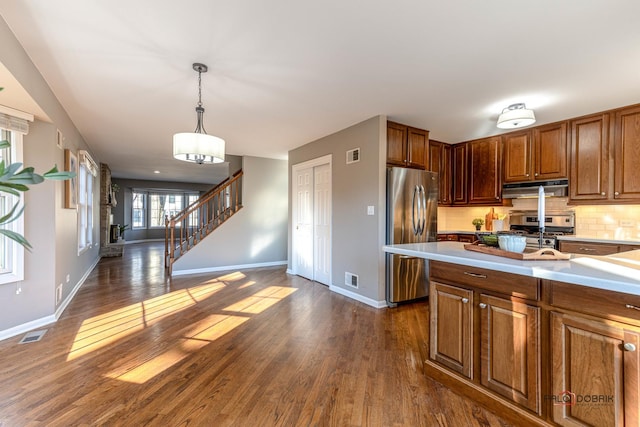 kitchen with dark wood-style floors, stainless steel appliances, light countertops, under cabinet range hood, and backsplash