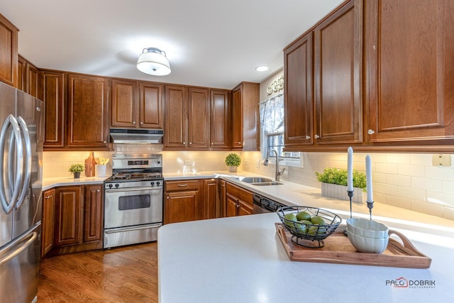 kitchen featuring dark wood-style floors, a sink, light countertops, under cabinet range hood, and appliances with stainless steel finishes