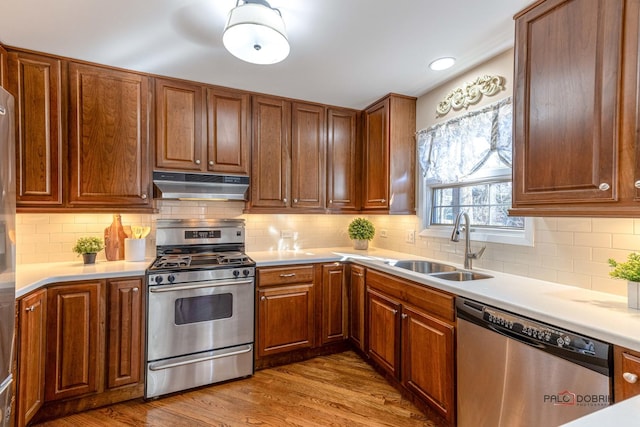 kitchen featuring under cabinet range hood, a sink, wood finished floors, appliances with stainless steel finishes, and light countertops