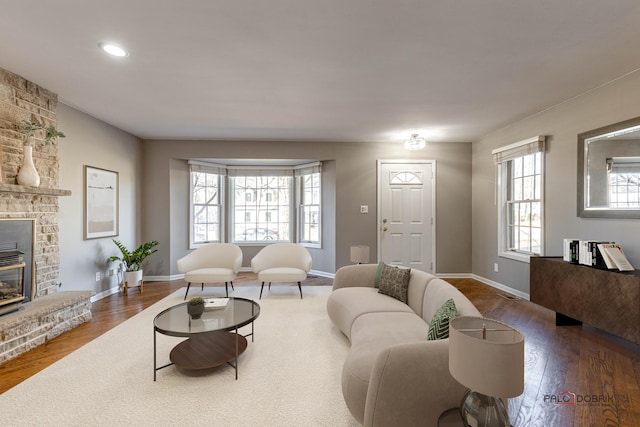 living room featuring a stone fireplace, recessed lighting, baseboards, and wood finished floors