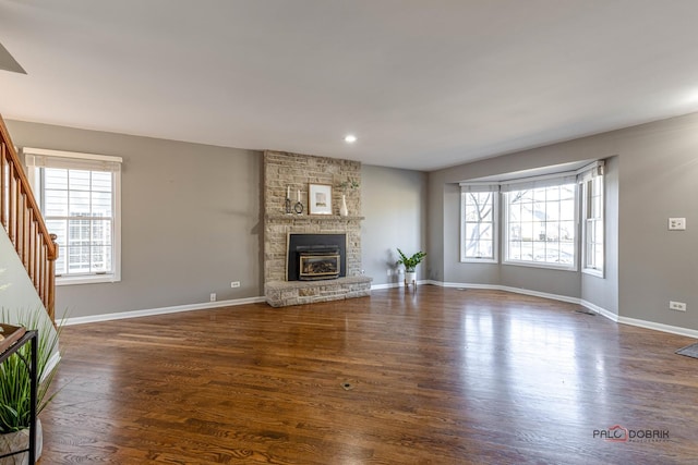 unfurnished living room featuring stairway, baseboards, a stone fireplace, and dark wood-style floors