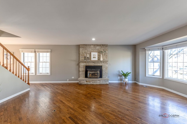 unfurnished living room with stairs, dark wood-style floors, a wealth of natural light, and a fireplace