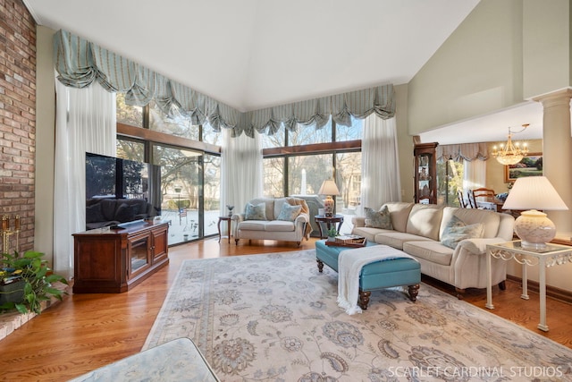 living room featuring ornate columns, high vaulted ceiling, a chandelier, and light hardwood / wood-style flooring