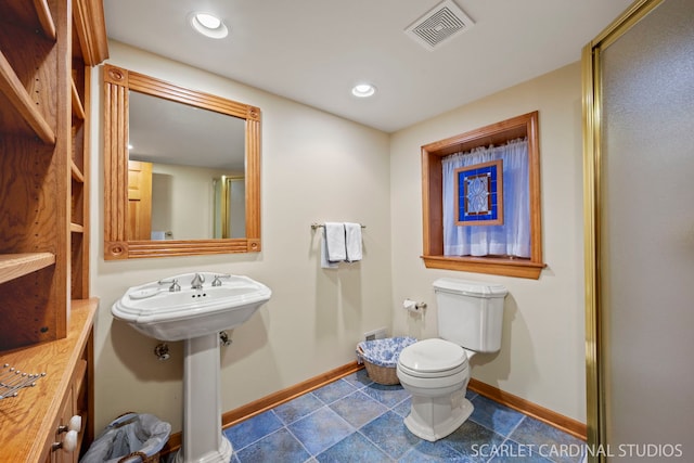 bathroom featuring toilet, a shower with shower door, and sink