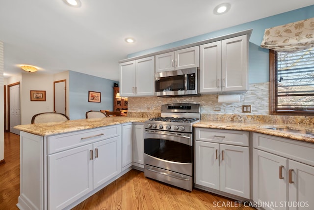 kitchen with stainless steel appliances, light hardwood / wood-style flooring, white cabinets, and kitchen peninsula