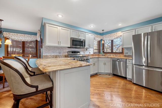 kitchen featuring pendant lighting, stainless steel appliances, kitchen peninsula, and white cabinets