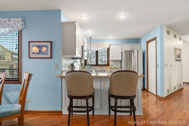 kitchen with appliances with stainless steel finishes, white cabinets, decorative backsplash, hanging light fixtures, and light hardwood / wood-style flooring