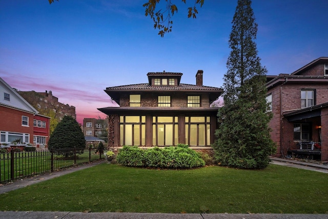 back house at dusk with a sunroom and a lawn